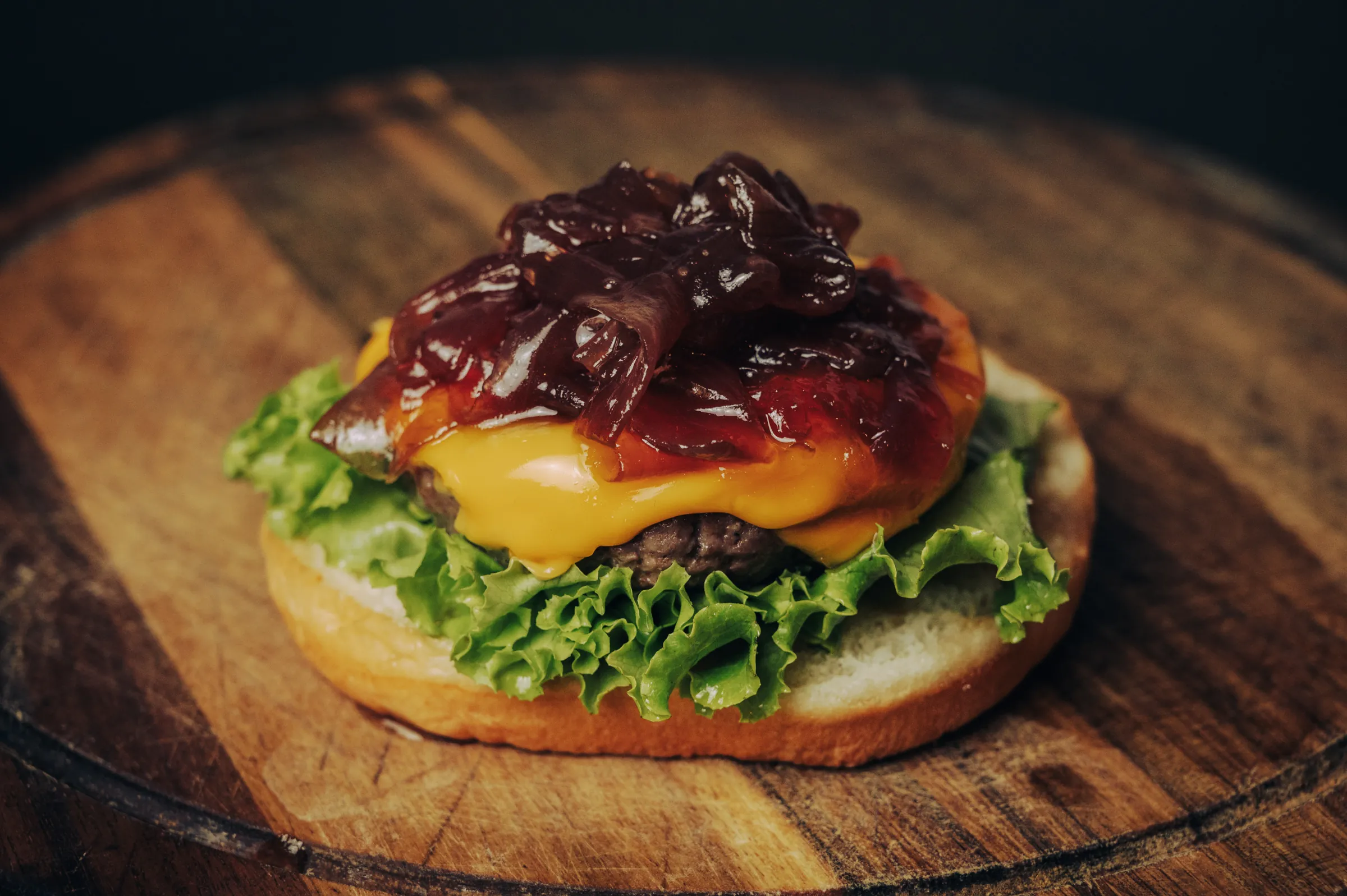 Offener Burger mit geschmolzenem Käse und karamellisierten Tropea-Zwiebeln auf einem Holzbrett