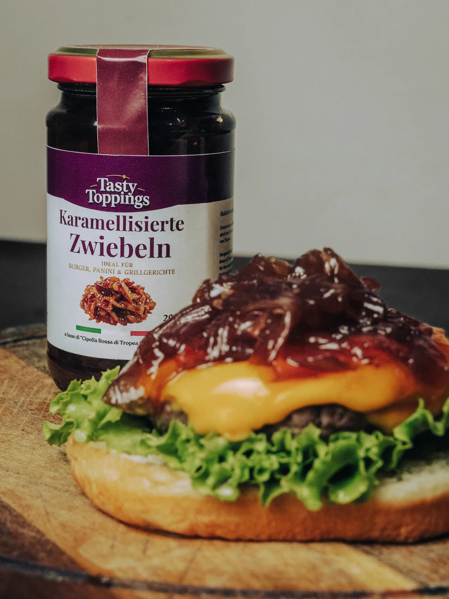 Das Glas Tasty Toppings Karamellisierte Zwiebeln, davor ein offener Burger mit Käse und karamellisierten Tropea-Zwiebeln