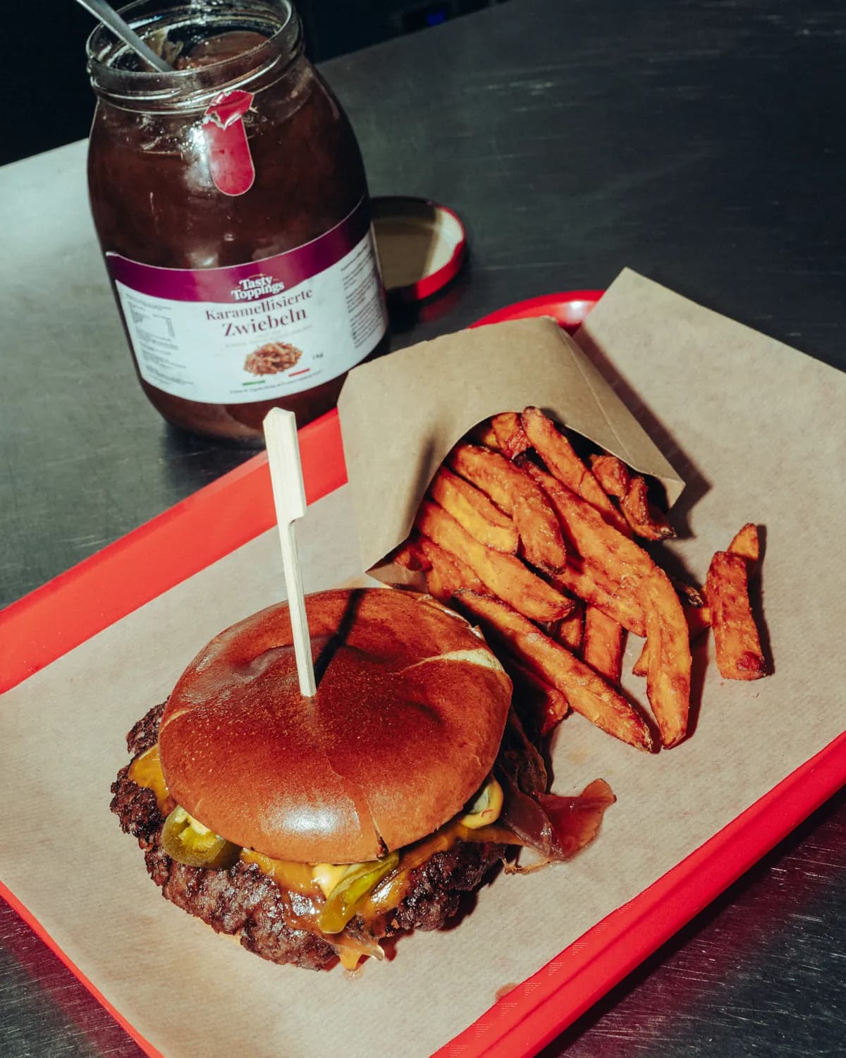 Burger mit karamellisierten Tropea-Zwiebeln und Süßkartoffel-Pommes auf einem roten Tablett